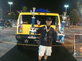 Man holding two trophies in front of his car